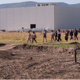 People walking on grass in front of a factory building. Biodiversity mapping of Kuklen Industrial Park with Municipality of Kuklen in the framework of the scientific exchange project New Ruralities Photo: Sandro Arabyan