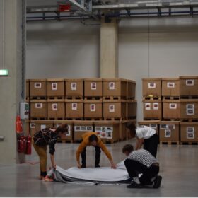 Students working in a factory room, boxes in the background. Newrope Design Studio «Smooth Operator(s)» in Odelo Factory, 2022