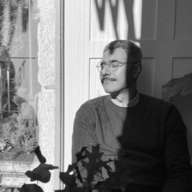 Portrait of Nitin Bathla, black and white, with closed eyes outside, in front of a house door.